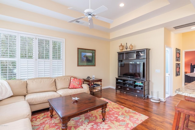 living room with a tray ceiling, dark wood-type flooring, and ceiling fan