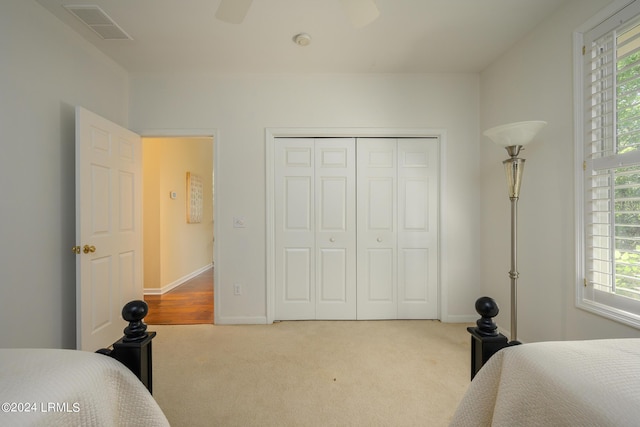 bedroom with light colored carpet, ceiling fan, and a closet