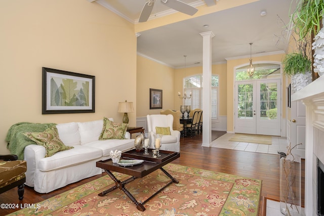 living room featuring hardwood / wood-style flooring, ornamental molding, ceiling fan with notable chandelier, french doors, and ornate columns