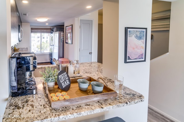 kitchen featuring light stone counters, light wood-type flooring, kitchen peninsula, and white refrigerator