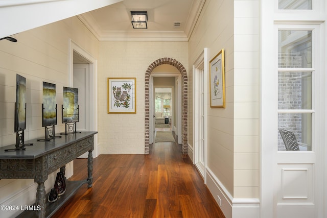 hall with dark hardwood / wood-style flooring, crown molding, and brick wall