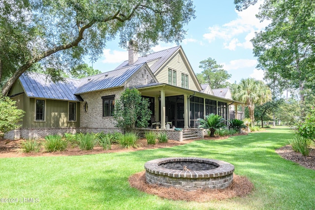 rear view of house with a sunroom, a lawn, and an outdoor fire pit