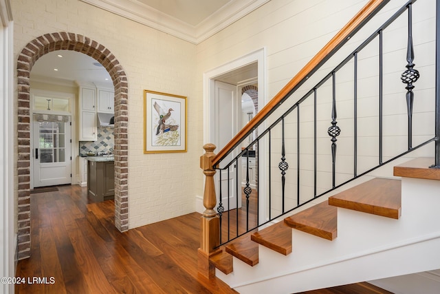 stairway featuring ornamental molding, brick wall, and wood-type flooring