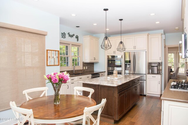 kitchen featuring a kitchen island, pendant lighting, sink, backsplash, and stainless steel appliances