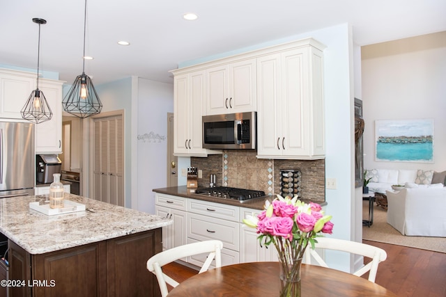 kitchen featuring appliances with stainless steel finishes, hanging light fixtures, tasteful backsplash, light stone counters, and dark hardwood / wood-style flooring