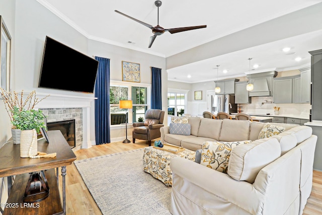 living area with a ceiling fan, crown molding, light wood-type flooring, a brick fireplace, and recessed lighting