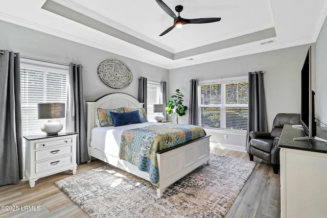 bedroom featuring light wood-type flooring, a tray ceiling, visible vents, and ornamental molding