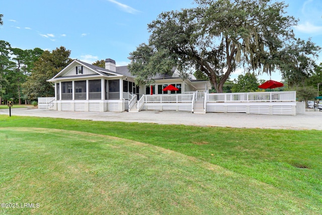 back of property featuring a lawn, a chimney, and a sunroom