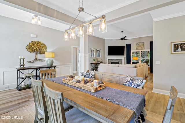 dining space with a ceiling fan, ornamental molding, a tiled fireplace, and wood finished floors