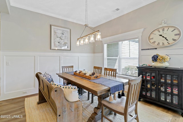 dining area with light wood-style floors, a wainscoted wall, crown molding, and visible vents