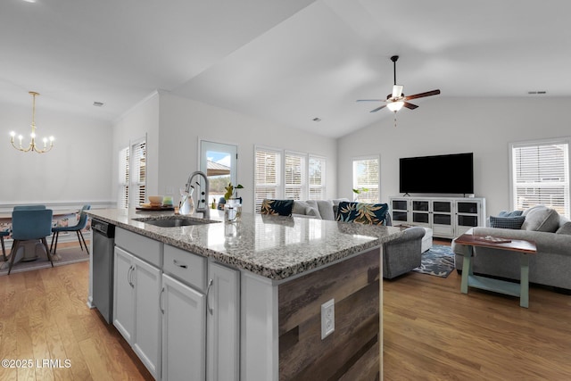 kitchen with sink, dishwasher, a kitchen island with sink, light stone countertops, and decorative light fixtures