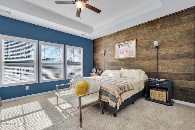 carpeted bedroom featuring a tray ceiling, ceiling fan, and wood walls