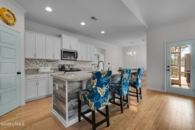 kitchen with a breakfast bar area, appliances with stainless steel finishes, a kitchen island with sink, white cabinets, and decorative light fixtures