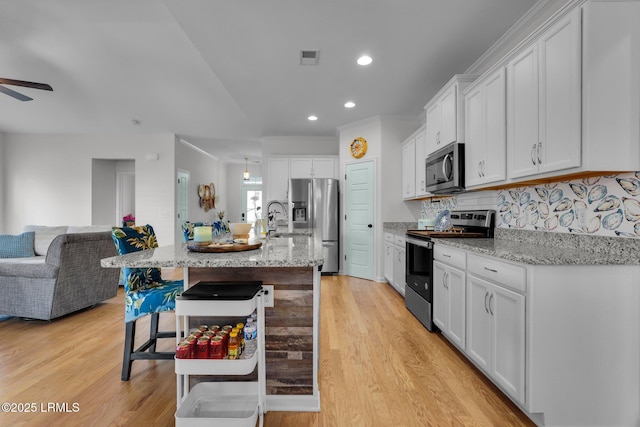 kitchen featuring an island with sink, appliances with stainless steel finishes, a breakfast bar, and white cabinets