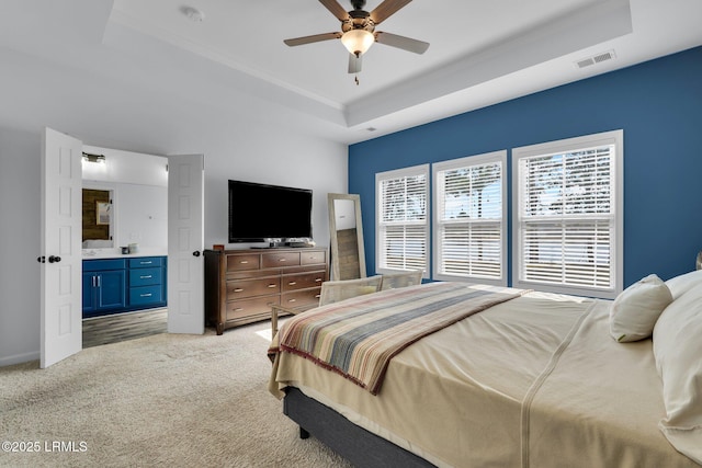 bedroom with light carpet, a raised ceiling, ceiling fan, and ensuite bathroom