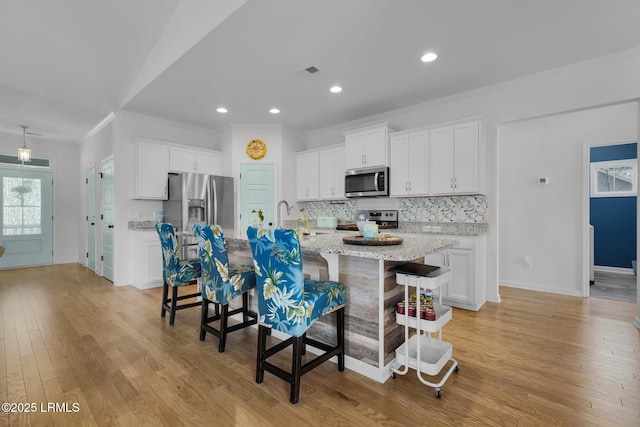 kitchen featuring a kitchen bar, an island with sink, stainless steel appliances, decorative backsplash, and white cabinets