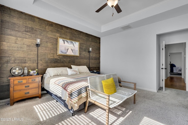 bedroom with wooden walls, light colored carpet, ceiling fan, a raised ceiling, and crown molding