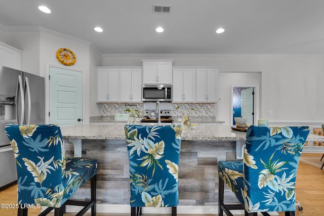 kitchen with stainless steel appliances, an island with sink, light stone countertops, and white cabinets