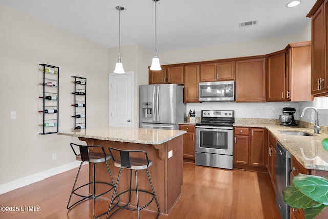 1216 Hearthstone Dr, Ridgeland, SC 29936 - kitchen with brown cabinetry, a center island, a sink, light stone counters, and stainless steel appliances