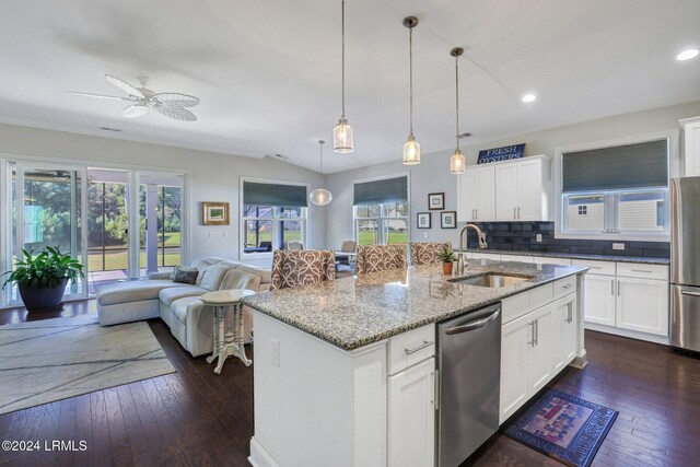 kitchen with sink, a kitchen island with sink, light stone countertops, white cabinets, and decorative light fixtures