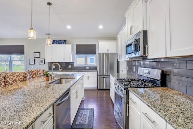 kitchen featuring appliances with stainless steel finishes, decorative light fixtures, white cabinetry, sink, and light stone counters