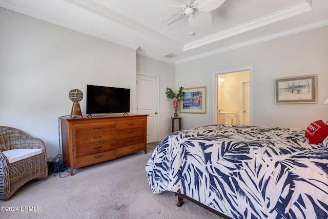 carpeted bedroom with a tray ceiling, ensuite bath, ornamental molding, and ceiling fan