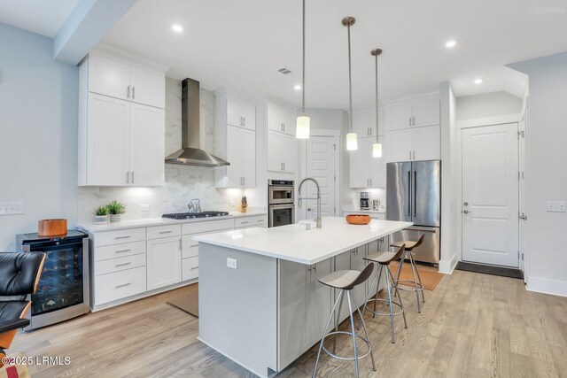 kitchen featuring tasteful backsplash, wall chimney exhaust hood, wine cooler, stainless steel appliances, and light wood-type flooring