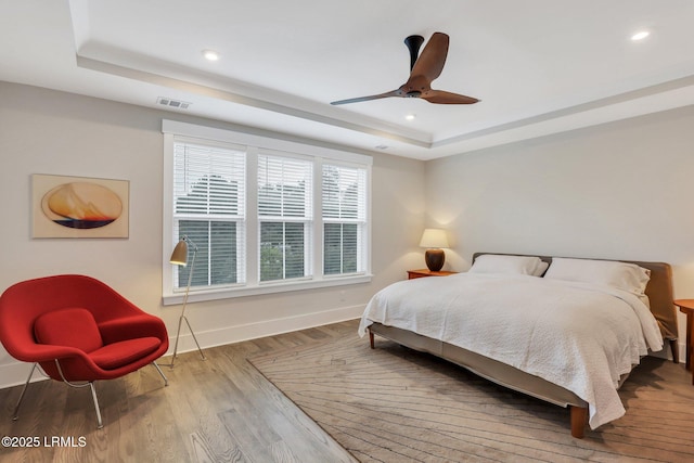 bedroom with a raised ceiling, visible vents, baseboards, and wood finished floors