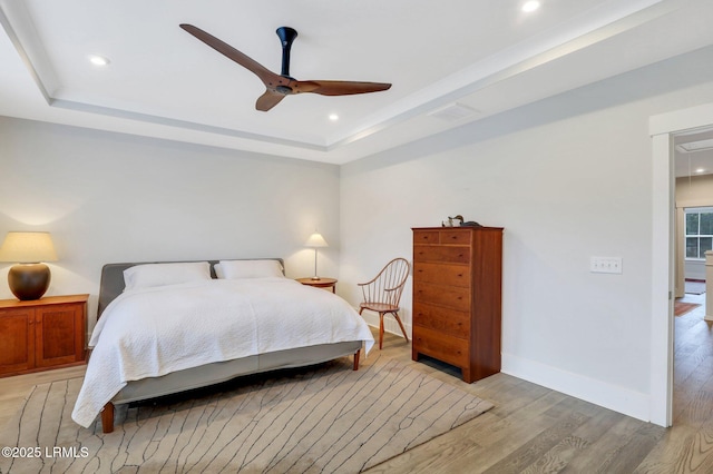 bedroom featuring light wood finished floors, a tray ceiling, recessed lighting, and baseboards