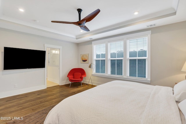 bedroom with baseboards, visible vents, a tray ceiling, and wood finished floors