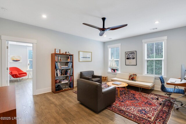 living area with a ceiling fan, wood finished floors, visible vents, and baseboards