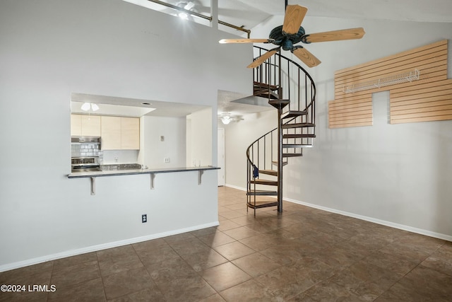 interior space with a breakfast bar area, ceiling fan, backsplash, high vaulted ceiling, and kitchen peninsula