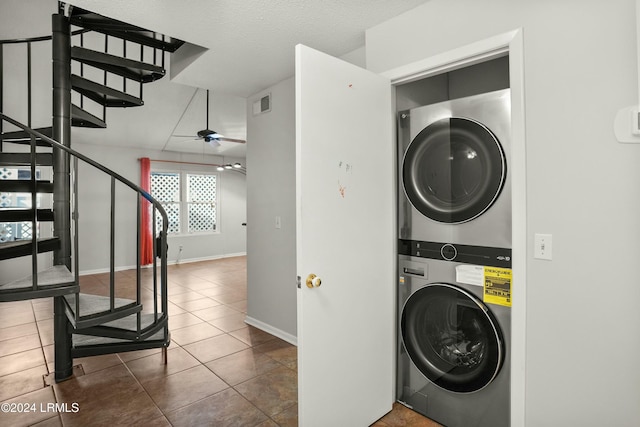 laundry room featuring dark tile patterned floors, stacked washer and clothes dryer, a textured ceiling, and ceiling fan