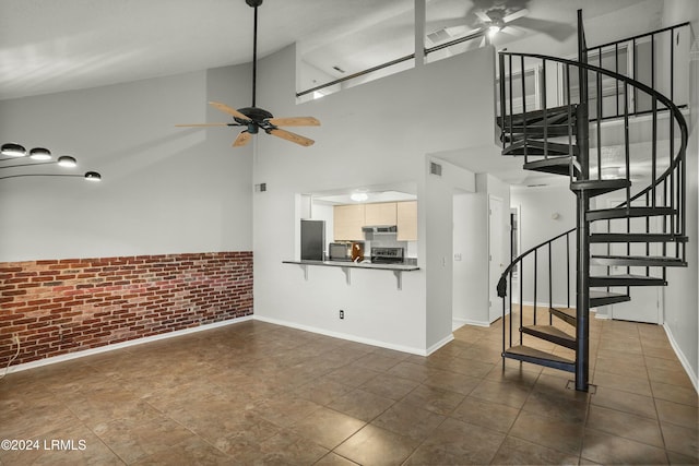 unfurnished living room with high vaulted ceiling, ceiling fan, and brick wall