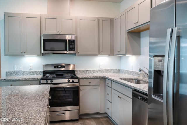 kitchen featuring sink, appliances with stainless steel finishes, gray cabinetry, light stone counters, and dark hardwood / wood-style flooring