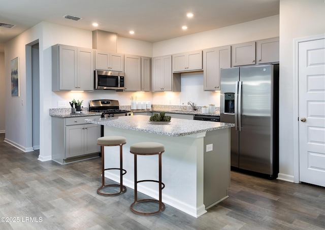 kitchen featuring appliances with stainless steel finishes, dark wood-type flooring, light stone countertops, a kitchen island, and sink