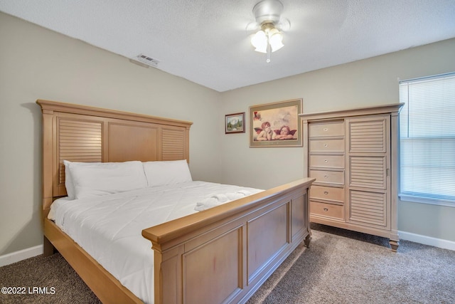 bedroom with a textured ceiling, dark colored carpet, visible vents, and baseboards