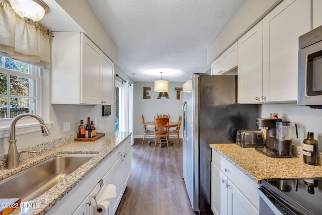 kitchen featuring stainless steel appliances, white cabinets, a sink, and decorative light fixtures