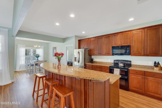 kitchen with light wood-style flooring, light stone counters, brown cabinets, black appliances, and a kitchen bar