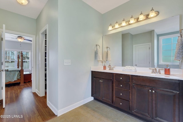 ensuite bathroom featuring double vanity, connected bathroom, baseboards, and a sink