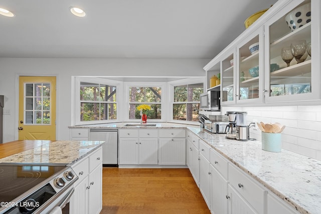 kitchen with white cabinets, backsplash, light hardwood / wood-style floors, stainless steel appliances, and light stone countertops