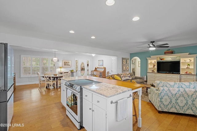 kitchen with a kitchen island, decorative light fixtures, white cabinets, stainless steel range with electric cooktop, and a kitchen bar