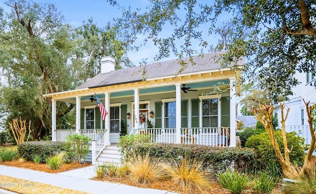 view of front of home featuring covered porch, ceiling fan, a chimney, and roof with shingles