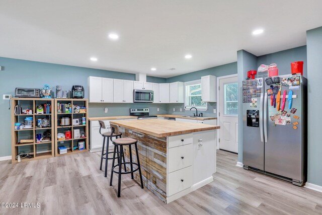 kitchen with wood counters, sink, a center island, appliances with stainless steel finishes, and white cabinets