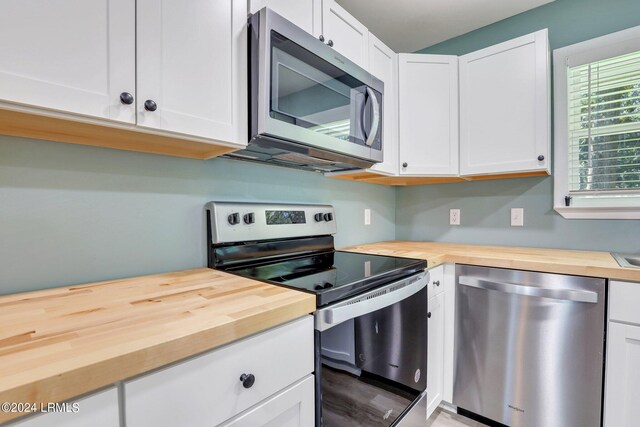 kitchen featuring stainless steel appliances, white cabinetry, and butcher block counters