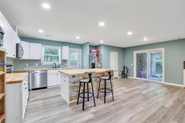 kitchen with butcher block counters, a kitchen bar, stainless steel appliances, white cabinets, and a kitchen island