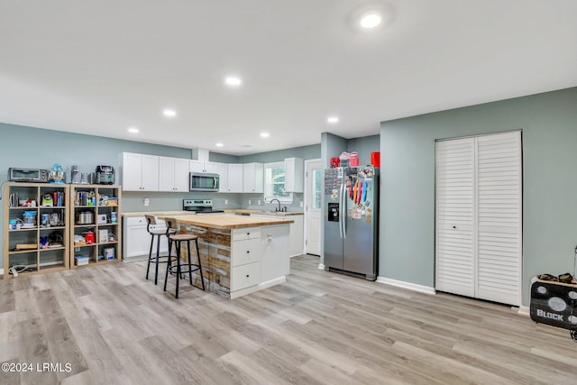 kitchen with wood counters, white cabinetry, a center island, appliances with stainless steel finishes, and a kitchen breakfast bar