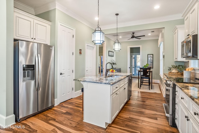 kitchen with stainless steel appliances, dark stone counters, a center island with sink, and white cabinets