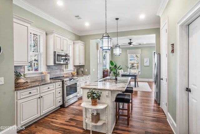 kitchen featuring sink, a center island with sink, dark stone countertops, stainless steel appliances, and white cabinets