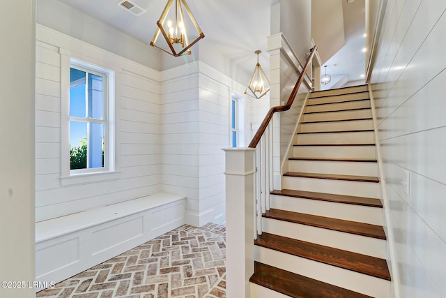 staircase featuring visible vents, brick floor, and an inviting chandelier